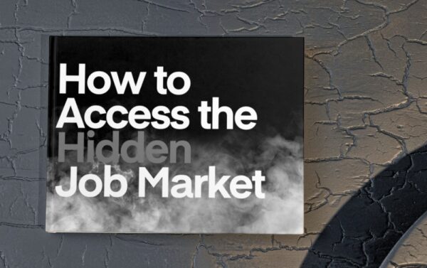 The image shows a black coffee table with a book on it. The book is landscape and the cover is black with grey smoke along the bottom half of the image. The title is How to Access the Hidden Job Market.