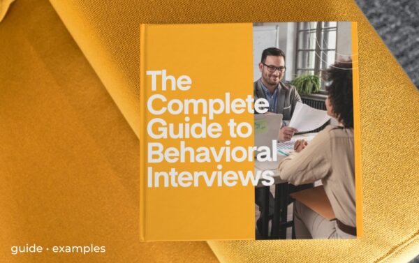 An orange square book sits on the arm of an orange chair. The book is titled The Complete Guide to Behavioral Interviews.