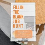 The image shows a book on a glass and wood table. The book is called Fill In The Blanks Job Hunt by Madeline Mann of Self Made Millennial