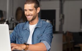 A man smiles as he writes a LinkedIn Headline on his laptop